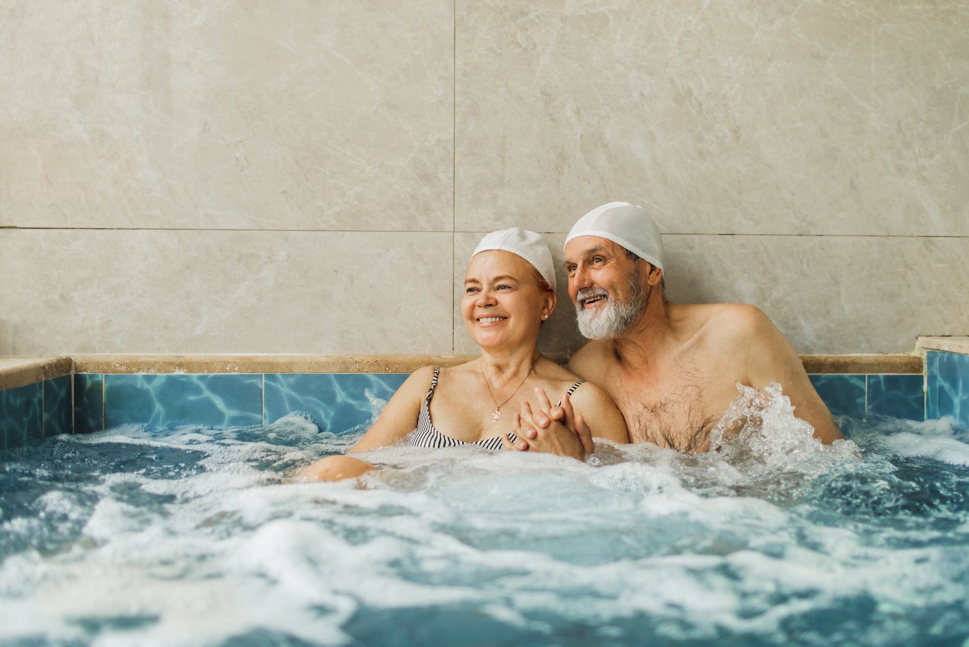 An elderly couple relaxes happily inside a tiled hot tub.