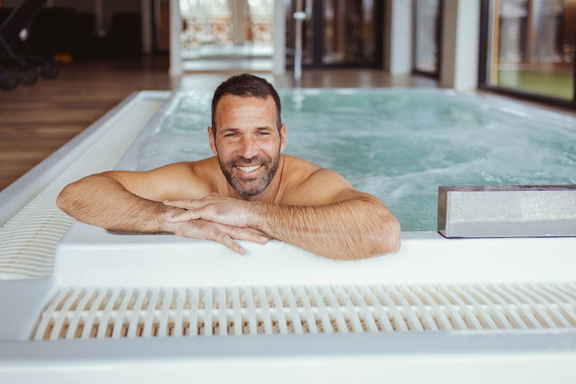 A man relaxes and smiles to the camera while relaxing in a hot tub.