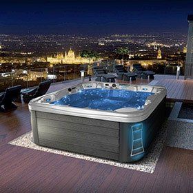 Hot tub on a deck overlooking a city skyline at night. Blue lights illuminate the water and exterior.