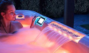 Woman in a glowing hot tub, interacting with a control panel near cascading water.