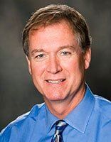 A man in a blue shirt and tie is smiling for the camera.