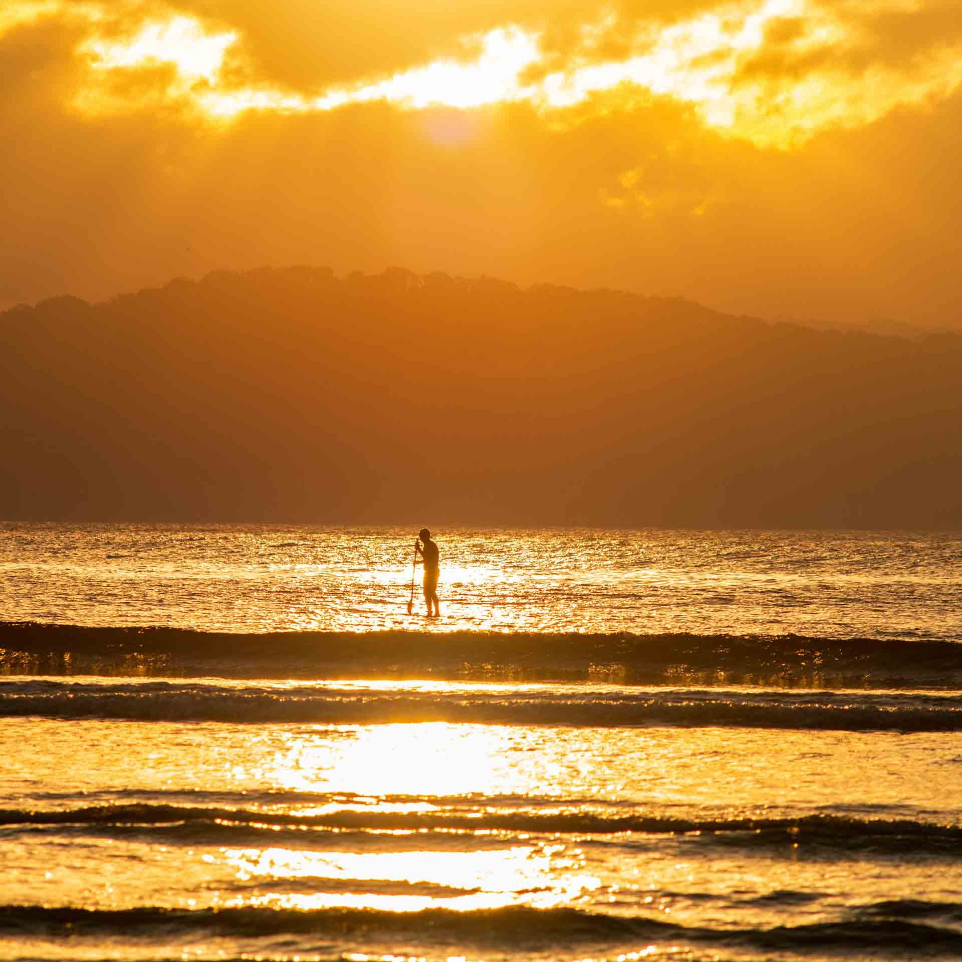 A Person is Standing on a Surfboard in the Ocean at Sunset — Slimes Boardstore in Umina Beach, NSW