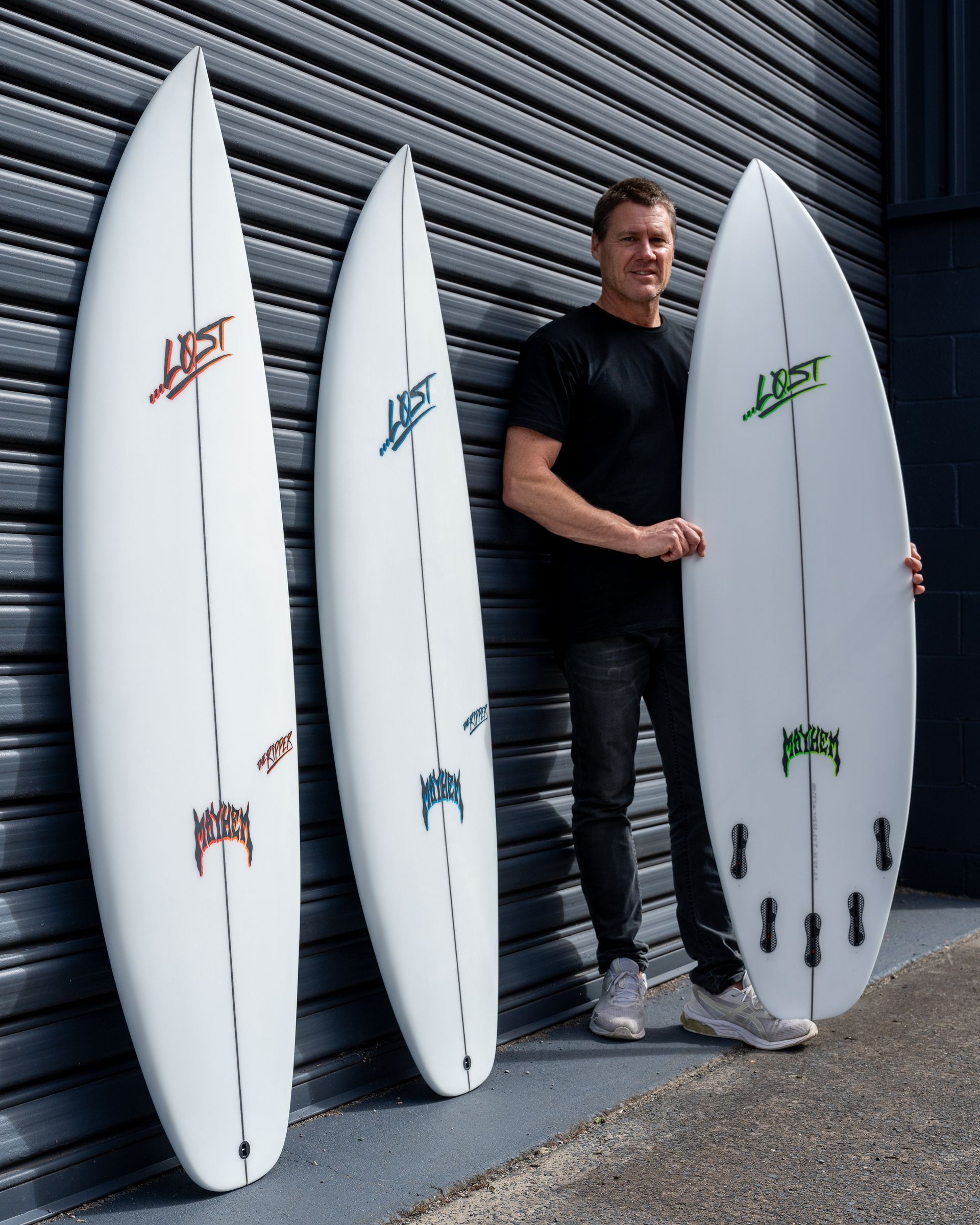 A Man is Holding Three Surfboards in Front of a Garage Door — Slimes Boardstore in Erina, NSW