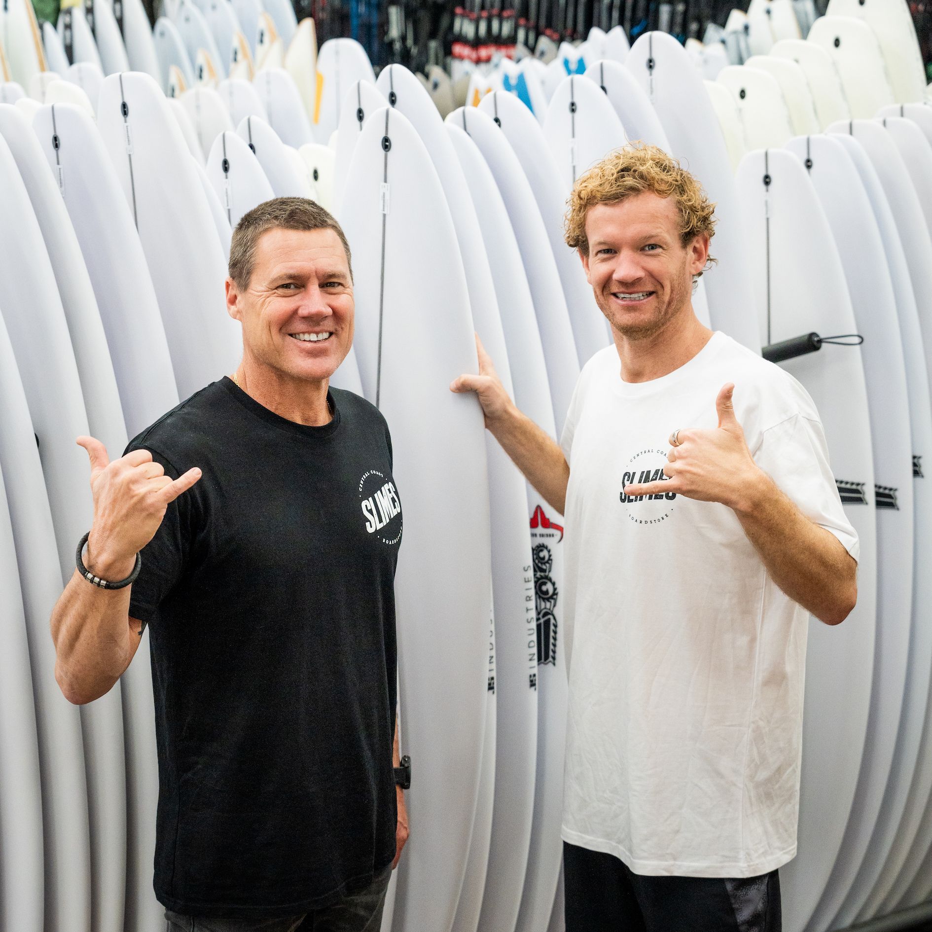 Two Men Are Standing Next to Each Other in Front of A Stack of Surfboards — Slimes Boardstore in Erina, NSW