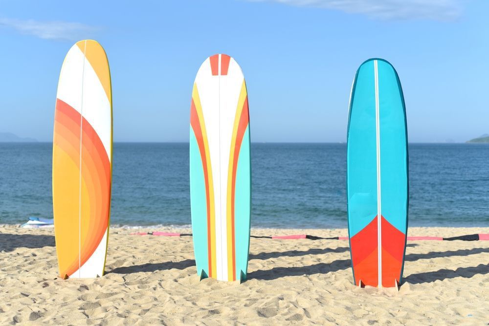 Surfboards resting on a sandy beach — Wetsuit in Erina, NSW