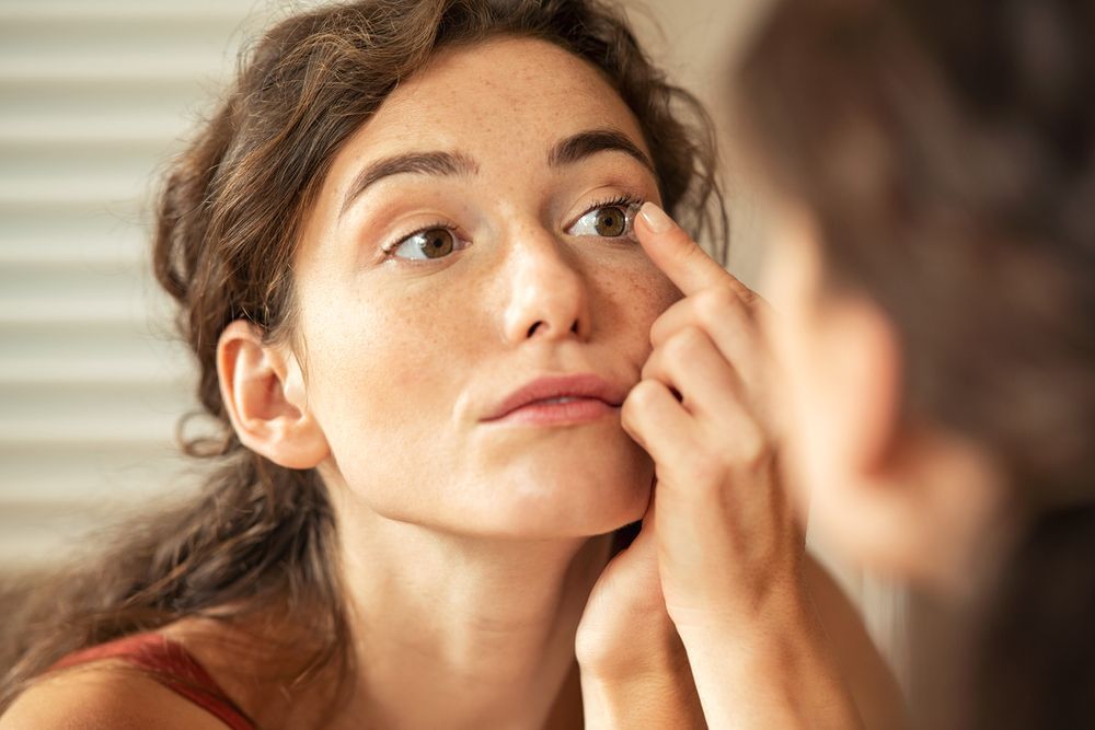 A Woman Is Looking at Her Face in The Mirror — John Williams Optometrist in Grafton, NSW