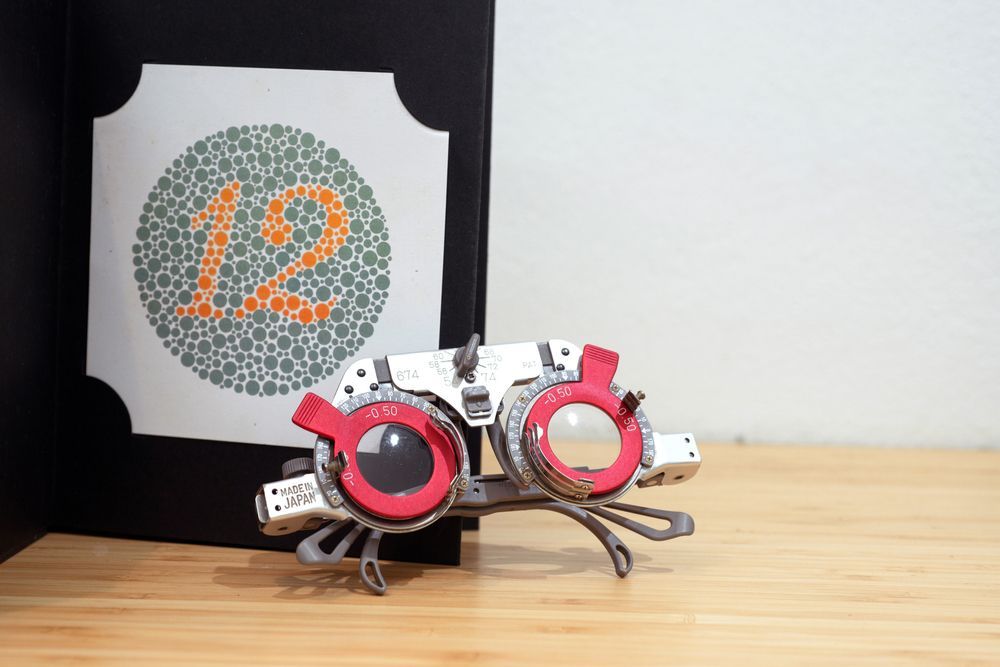 A Pair of Glasses Is Sitting on A Wooden Table Next to A Picture of A Color Blind Test — John Williams Optometrist in Grafton, NSW