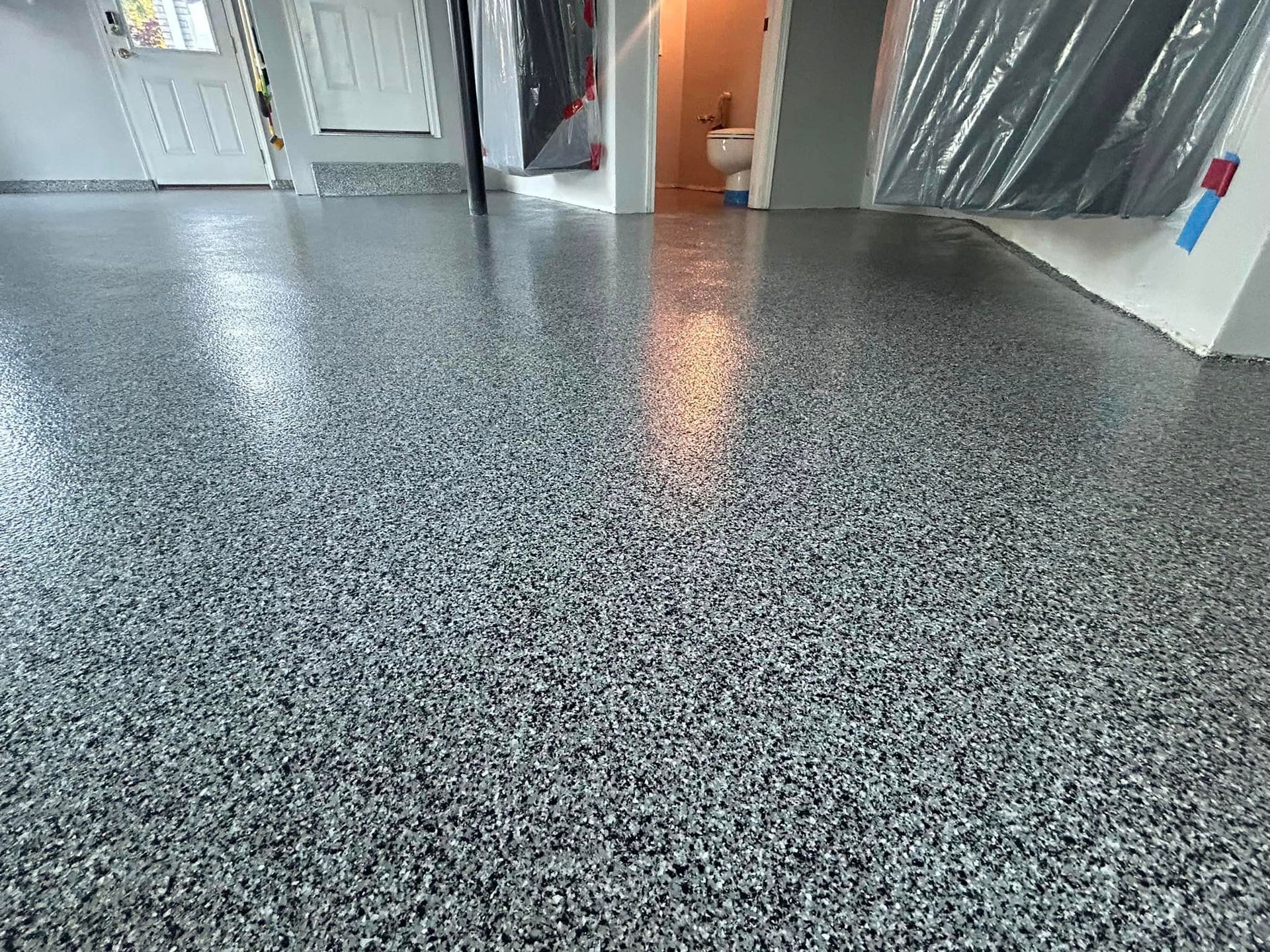 A gray concrete floor in a basement with a toilet in the background.