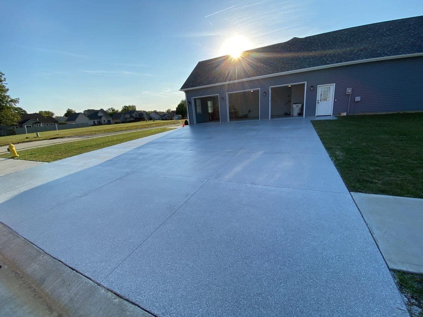 A driveway leading to a garage with the sun shining through the garage doors.