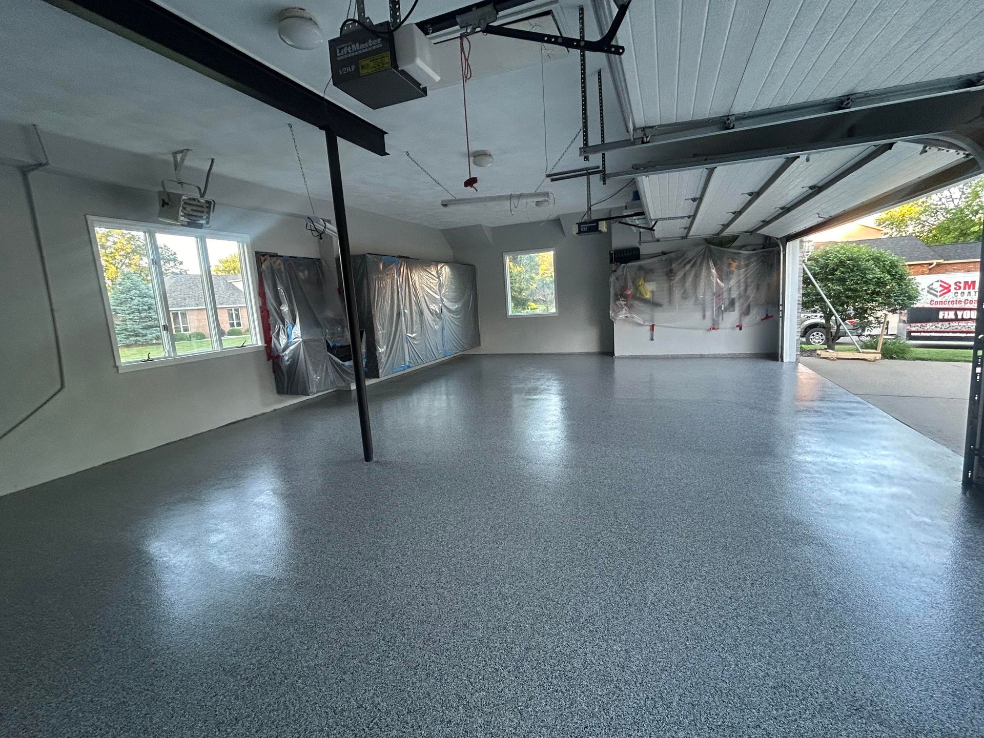An empty garage with a gray floor and a garage door open.