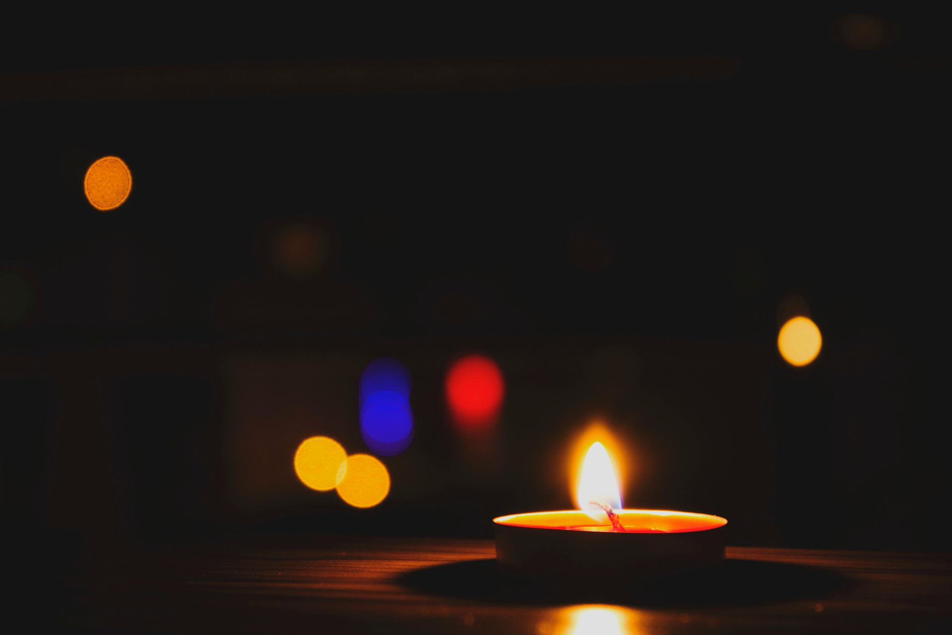 A lit candle is sitting on a wooden table in the dark.