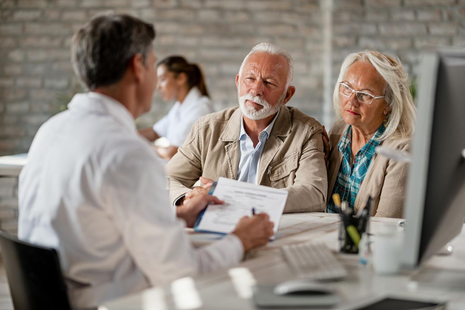 Three people in a meeting, discussing paperwork at a table in a bright office.