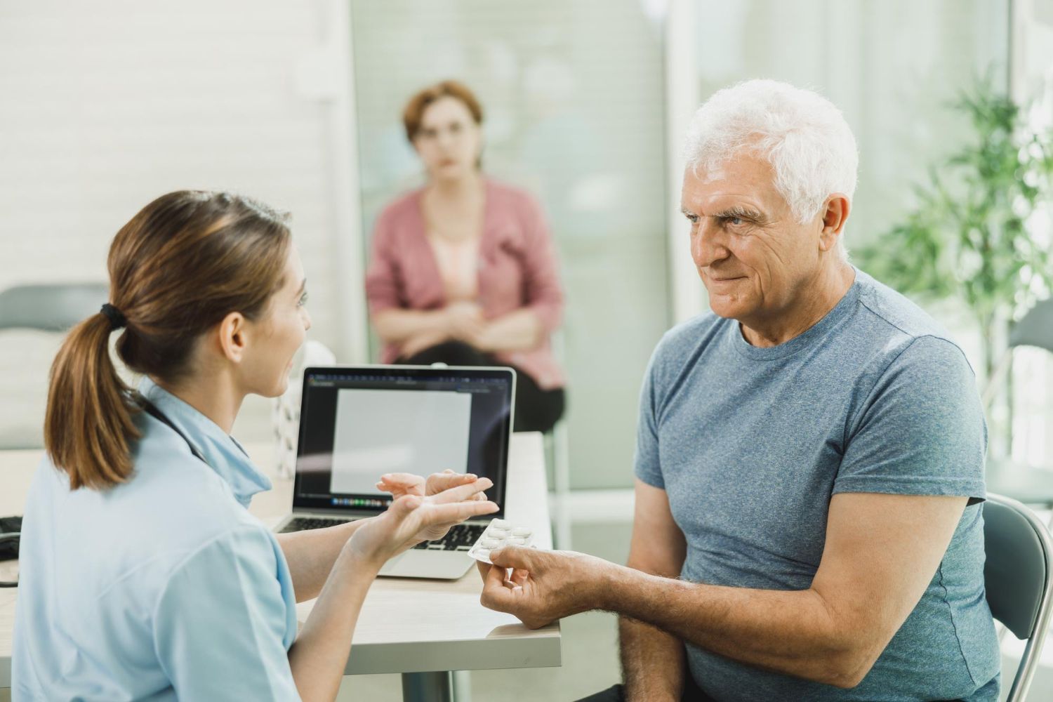 Healthcare worker showing paperwork to a patient while another person waits in a clinic reception area