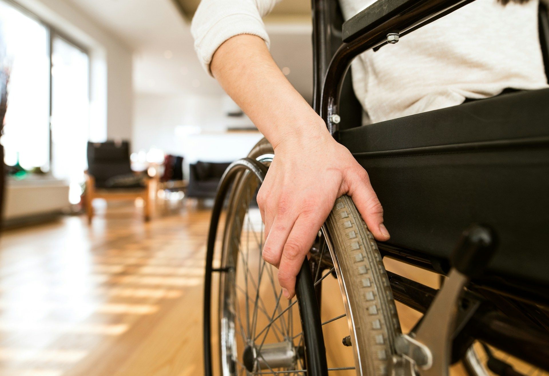 Hand resting on a wheelchair wheel in a sunlit room