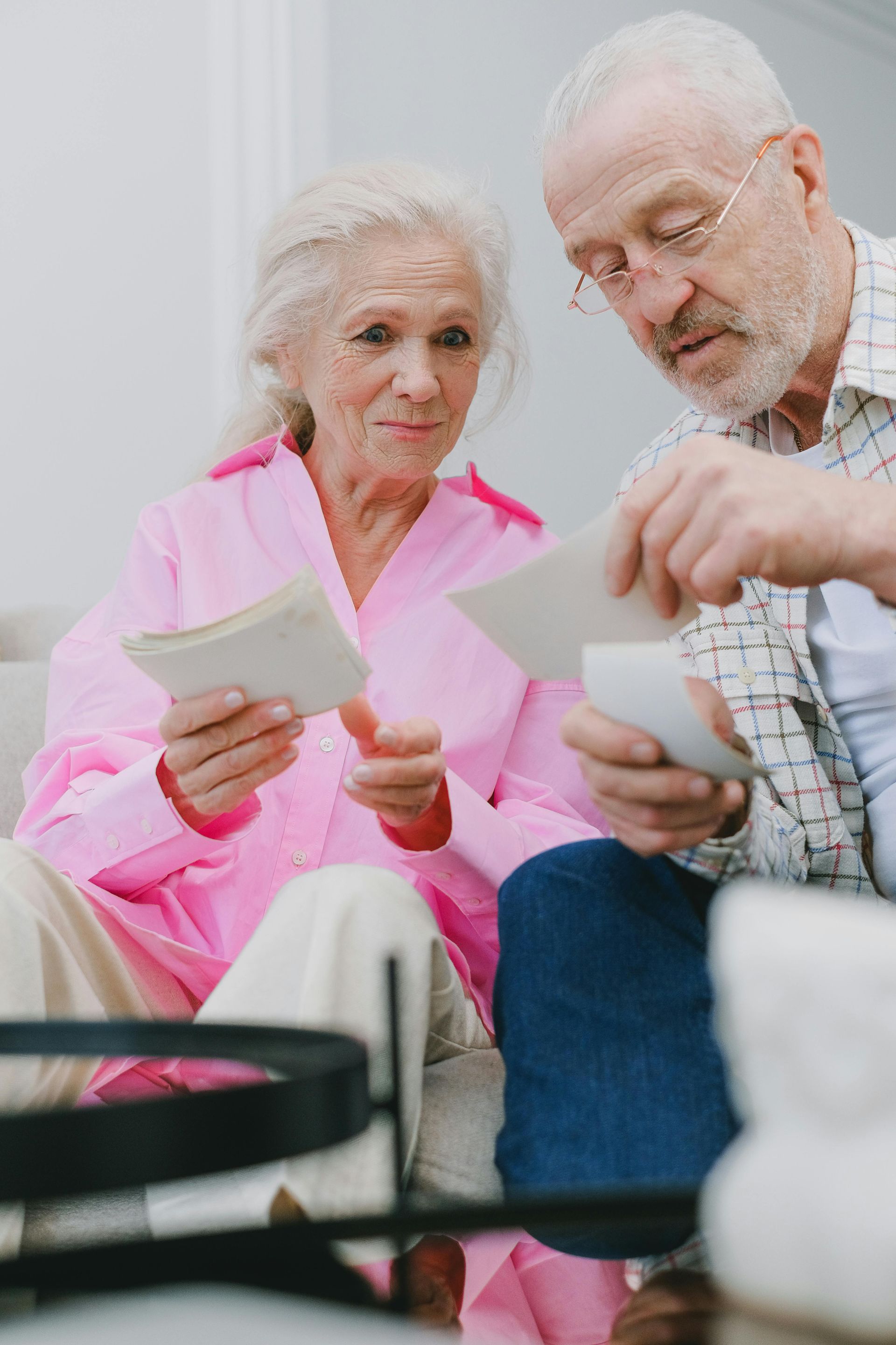 Two elderly people sit together, looking at photos and smiling in a bright living room.