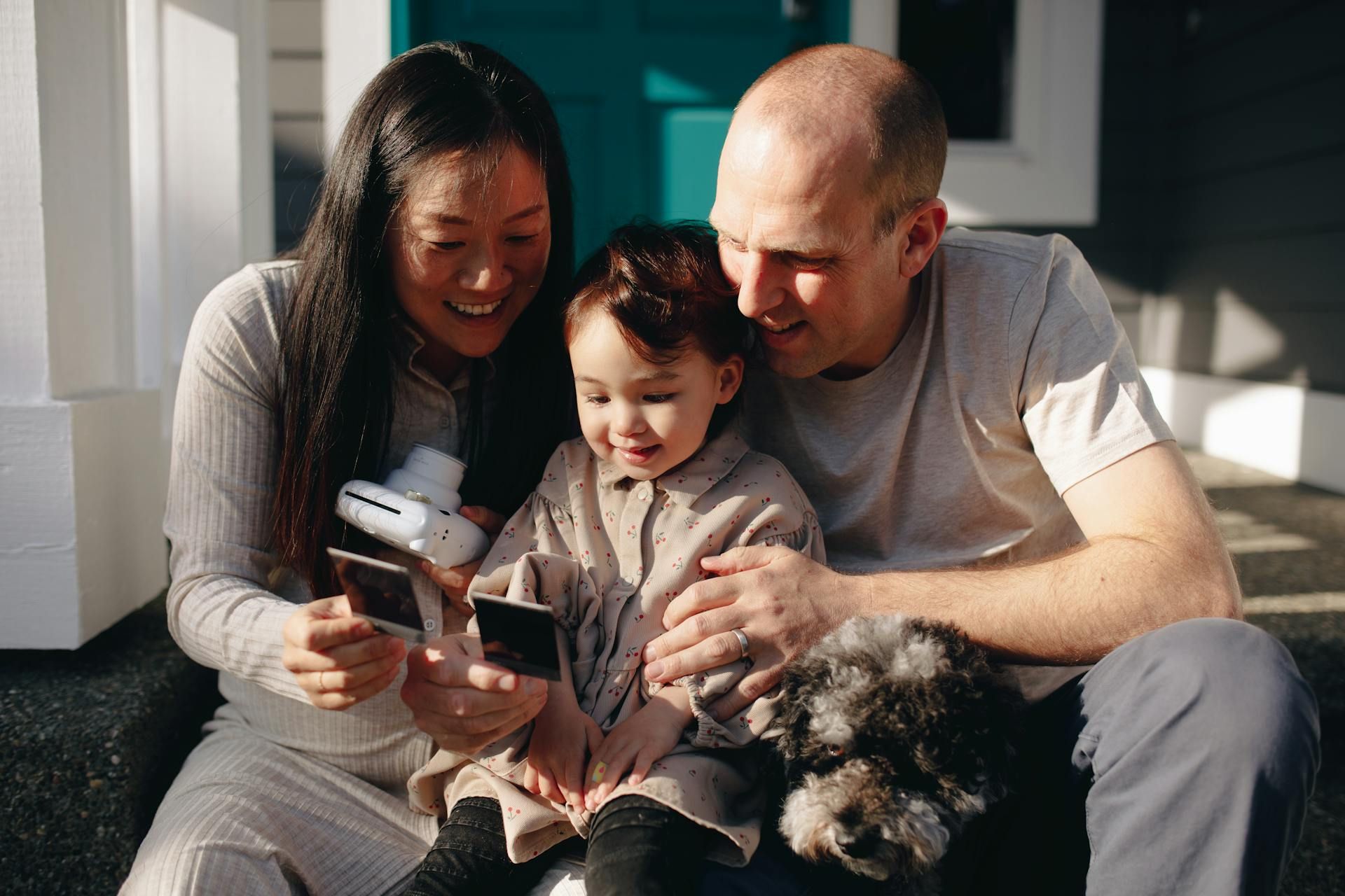 Family sitting on a couch, smiling and looking at a tablet with a small dog nearby