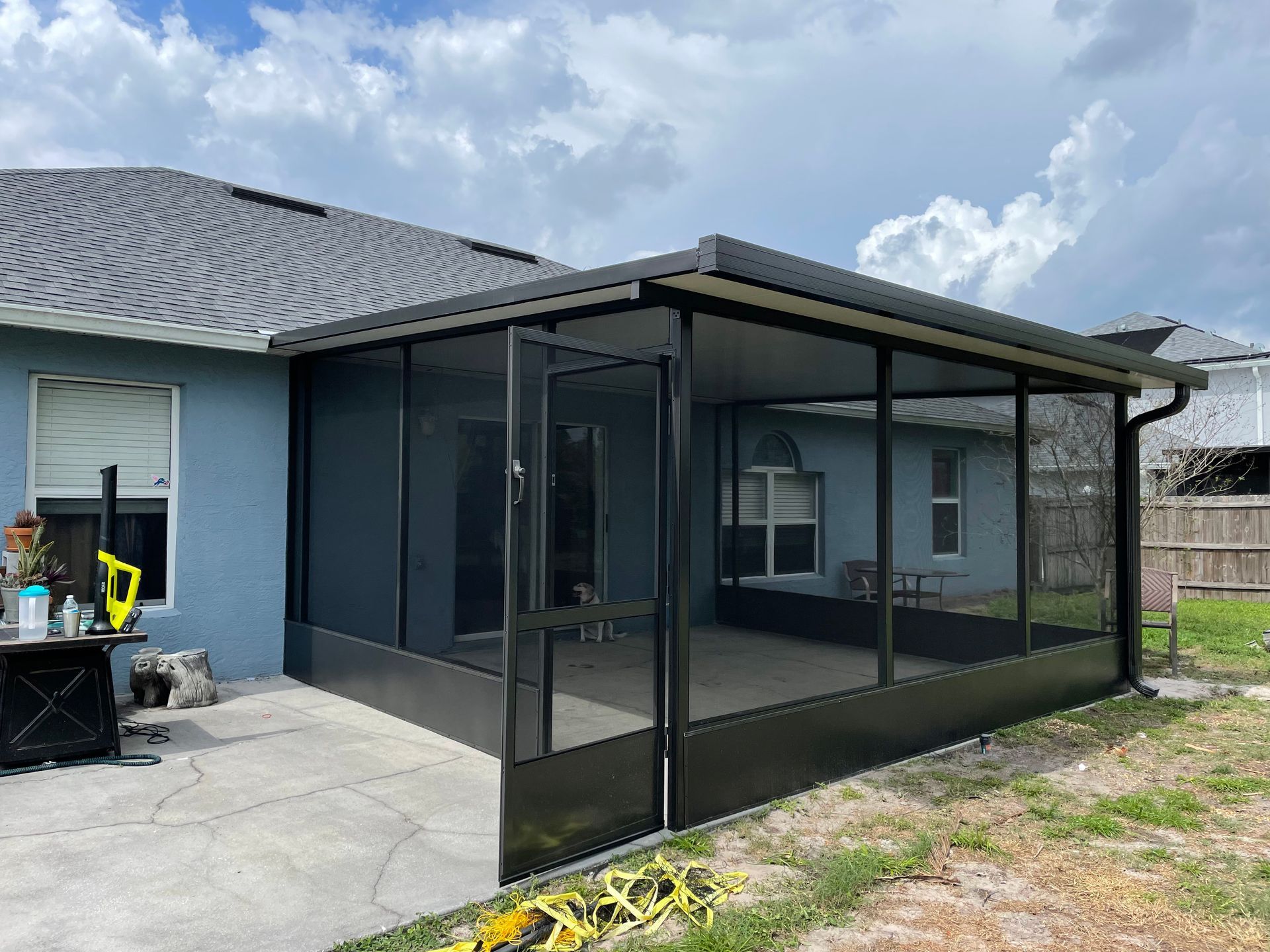 A screened-in patio enclosure attached to the back of a light blue house with a grey shingled roof.