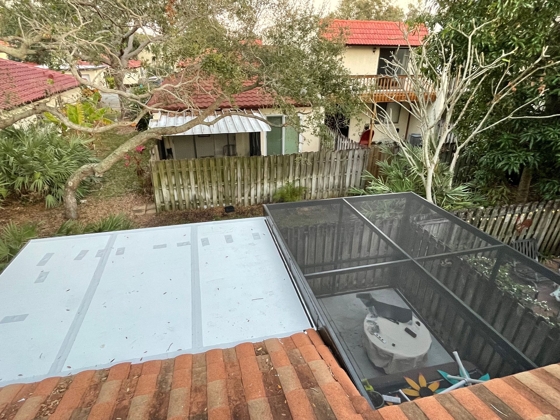 View from a tiled roof showing a gray flat roof section next to an enclosed screened patio with a small table inside.