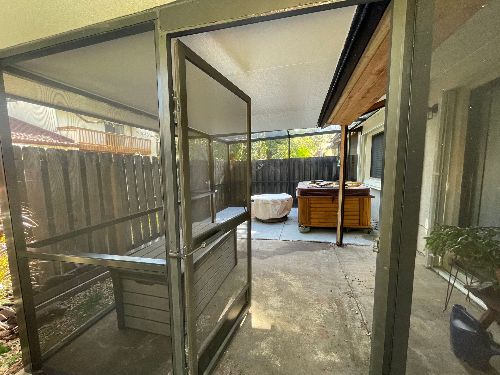 A covered patio with a screened-in area, featuring a wooden hot tub and a separate, draped circular object on the ground.