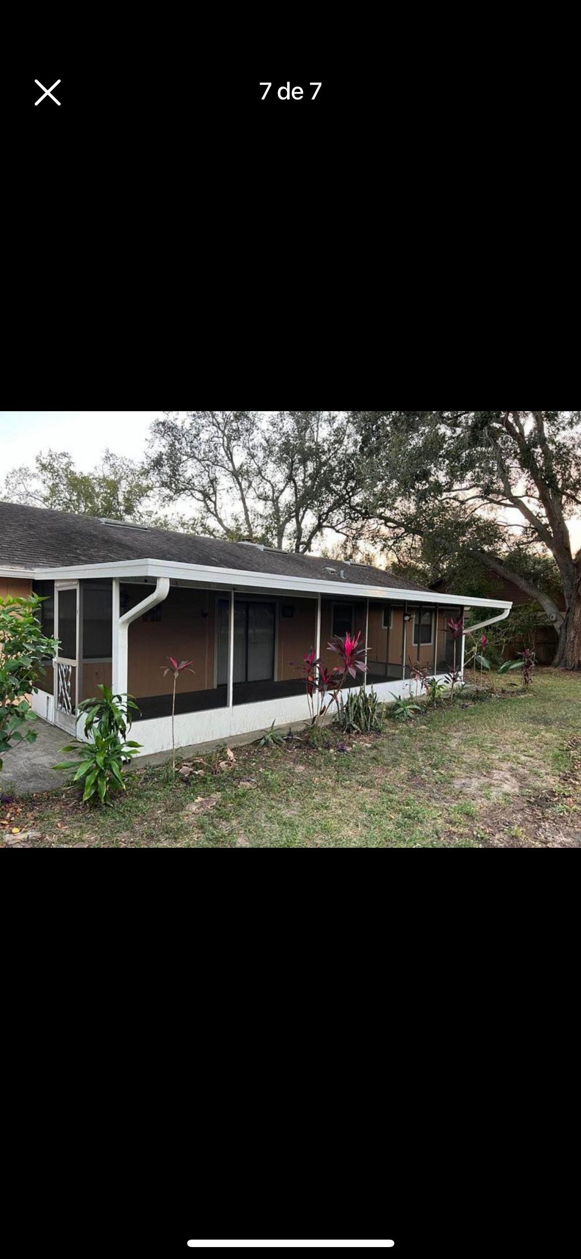 A side view of a single-story brick house with a white roof trim, covered porch, and surrounding lawn and trees.