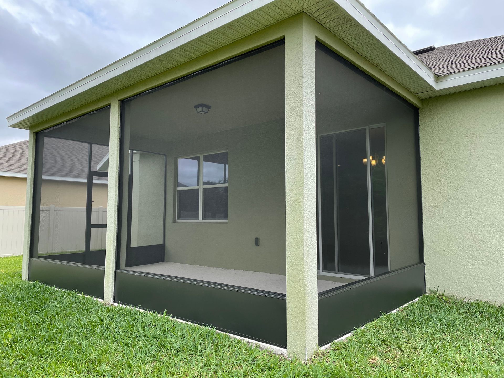 A green stucco house featuring a screened-in patio with dark framing, overlooking a lawn.