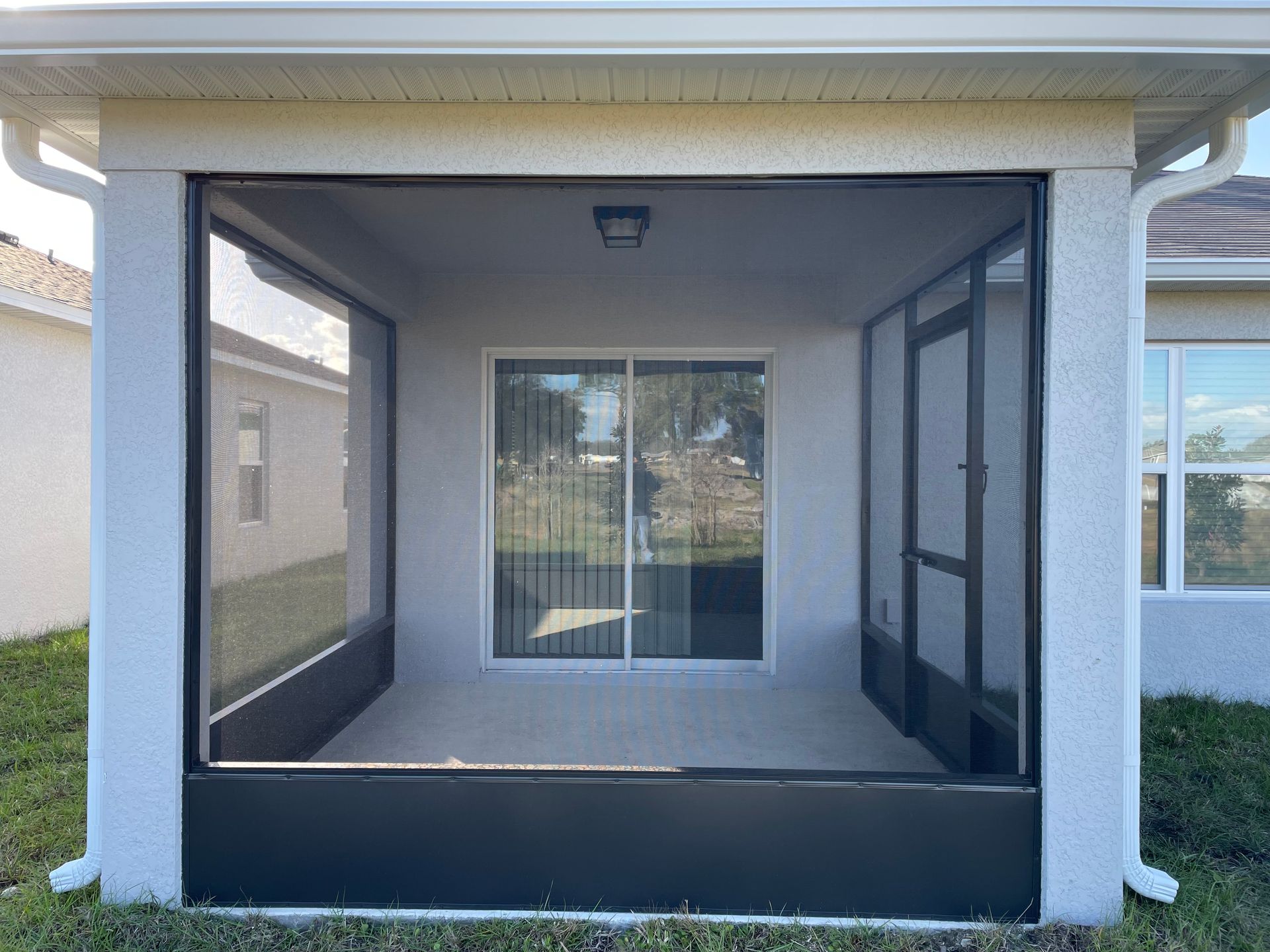 A covered patio enclosure featuring black framed screens, a sliding glass door, and a screen door set against a house.