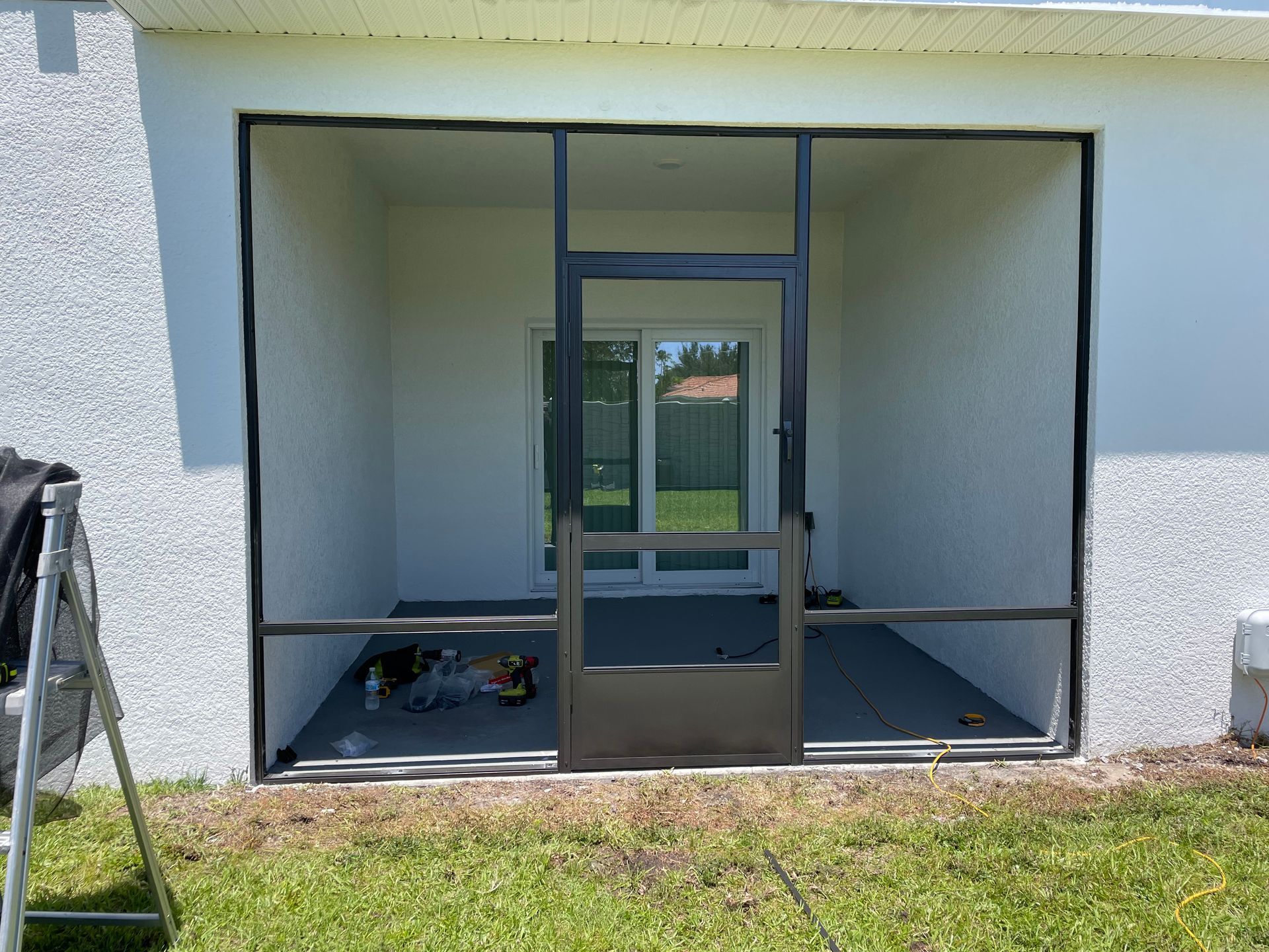 A newly installed dark-framed screen door and enclosure on a residential patio with white stucco walls.