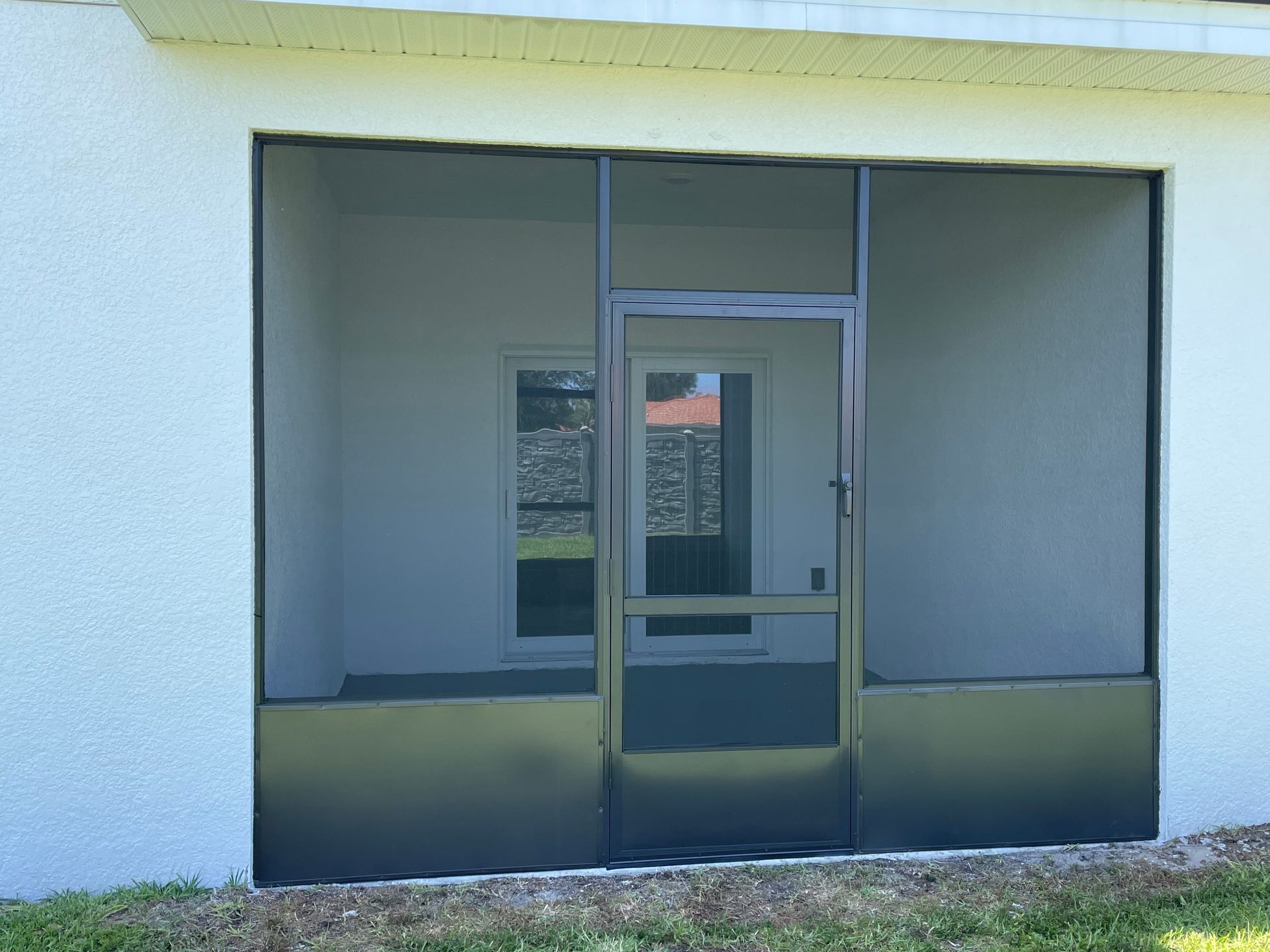 A dark-framed screened-in patio door with solid panels on the lower portion, set against a white stucco house exterior.