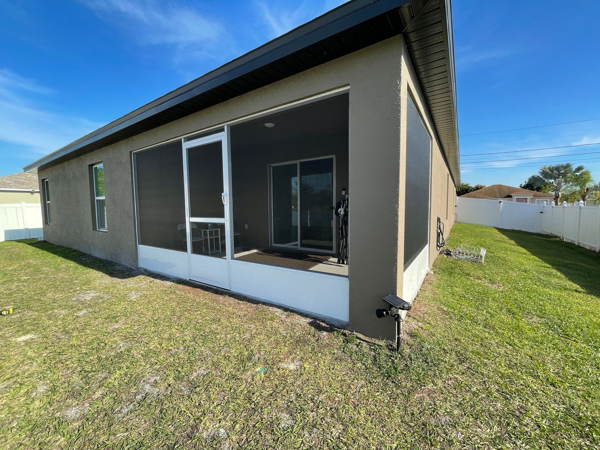 Exterior view of a tan house with a screened-in back porch, a white screen door, and a sliding glass door.