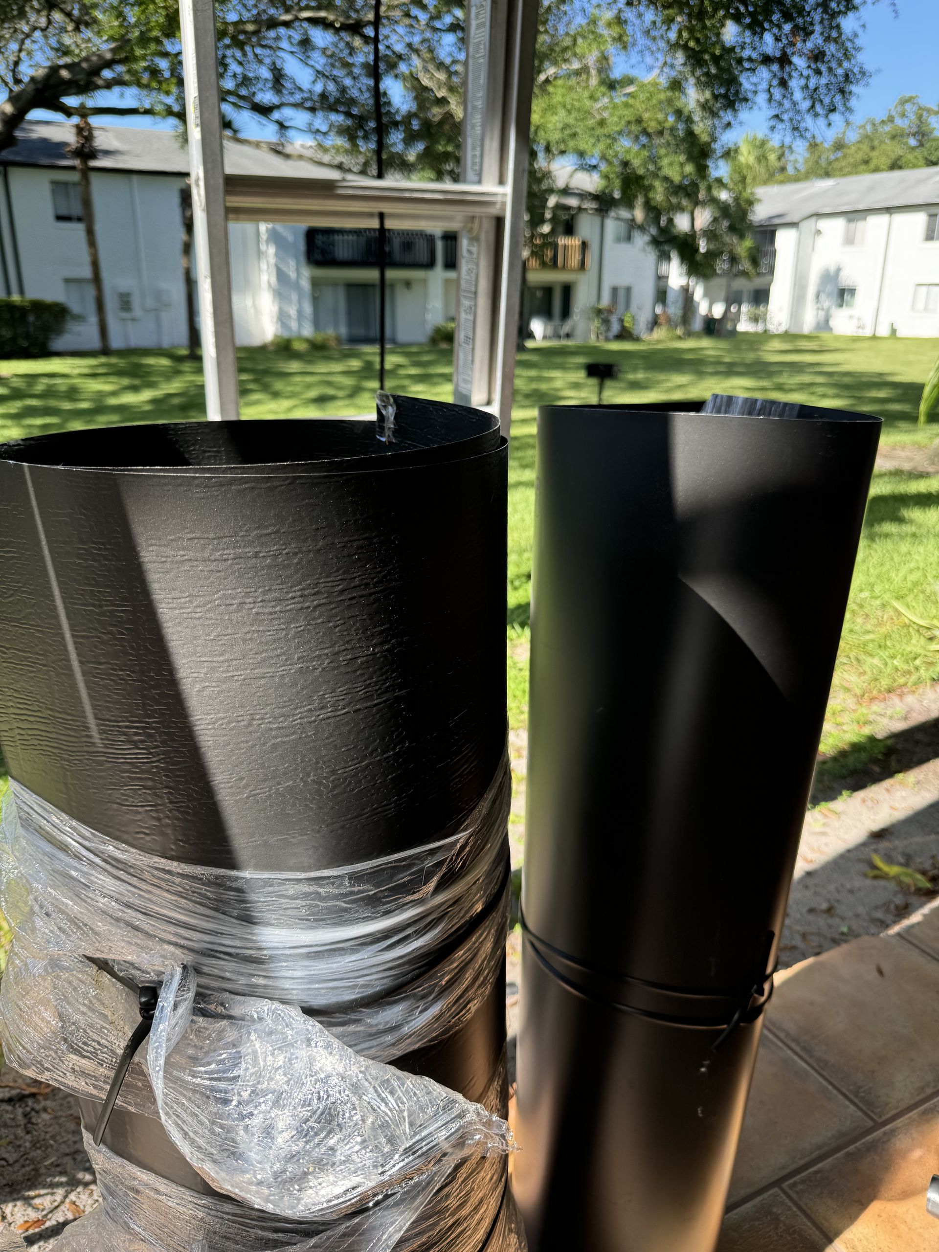 Two black cylindrical objects stand outdoors, one with a rough, textured surface and the other smooth, under bright sun.