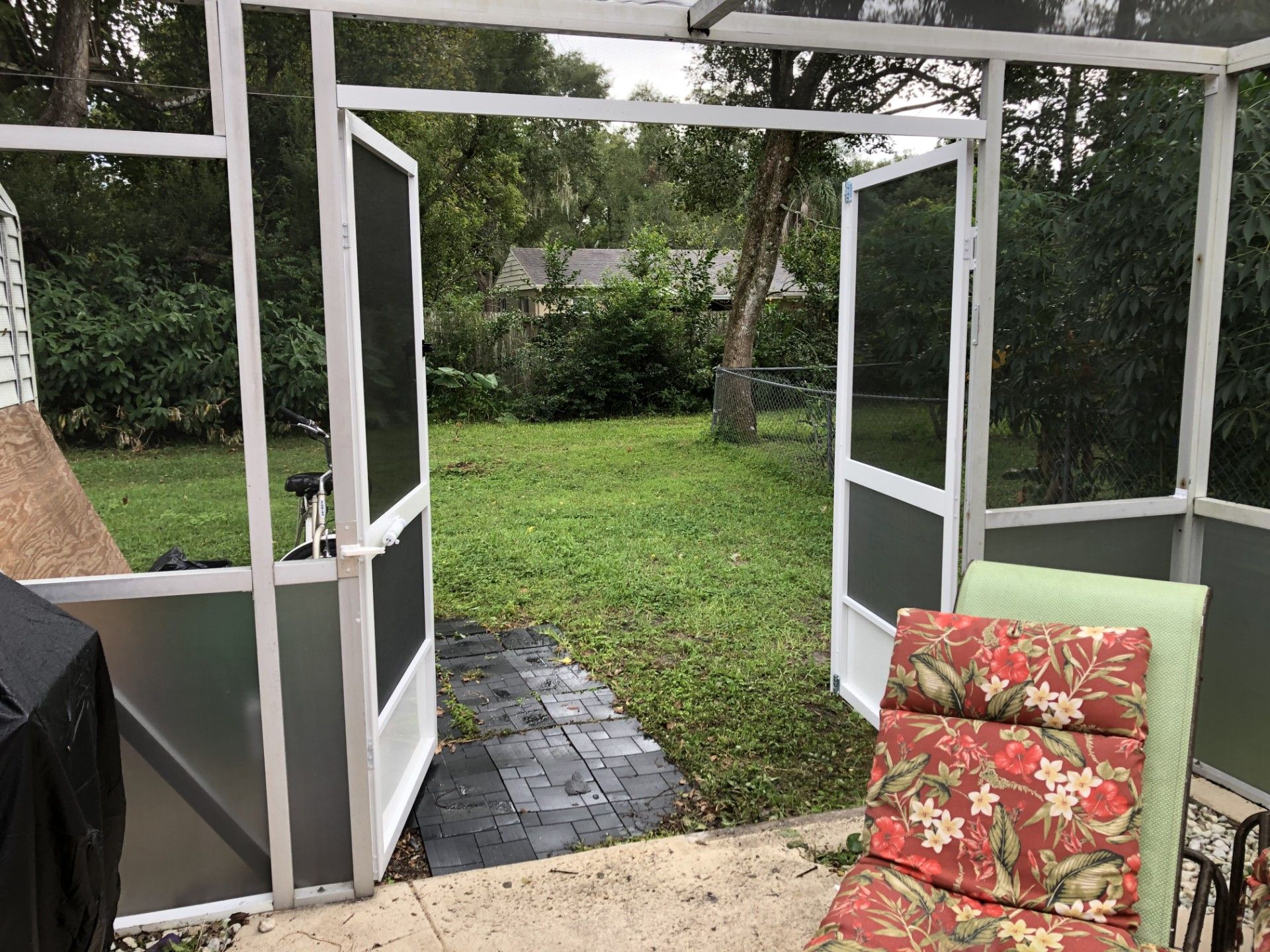Open white-framed screen doors lead from a screened-in patio to a grassy backyard with a stone path.
