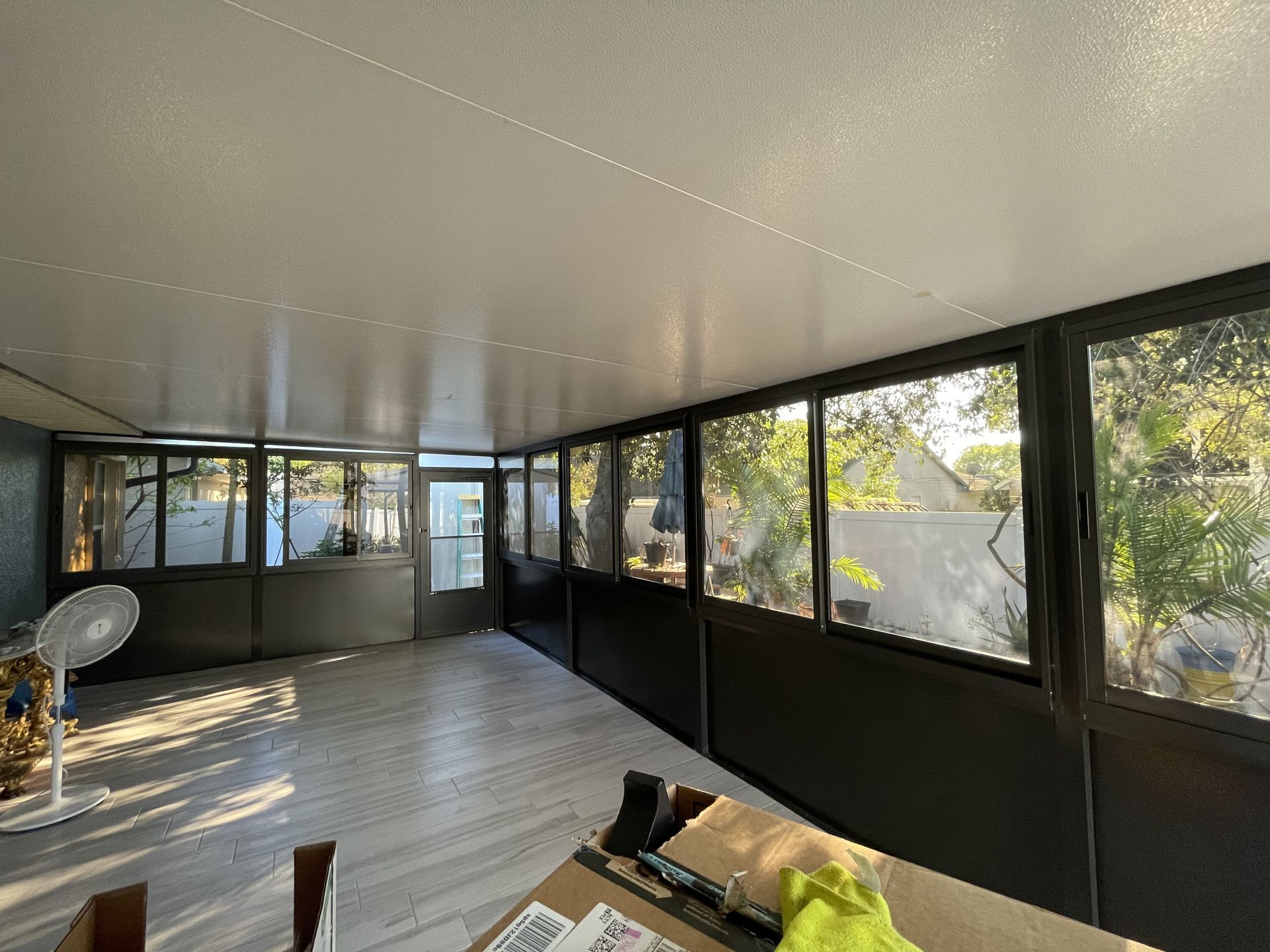 A bright, enclosed sunroom with large windows, a white ceiling, and light wood-plank flooring.