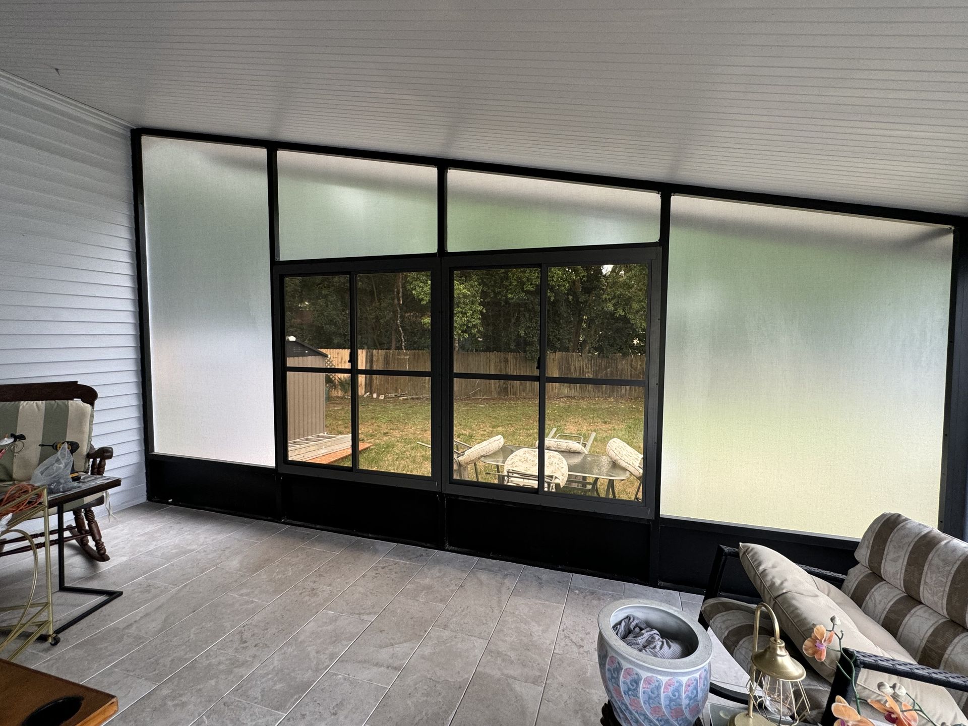 A sunroom featuring frosted upper windows and clear sliding glass doors looking out onto a backyard with outdoor furniture.