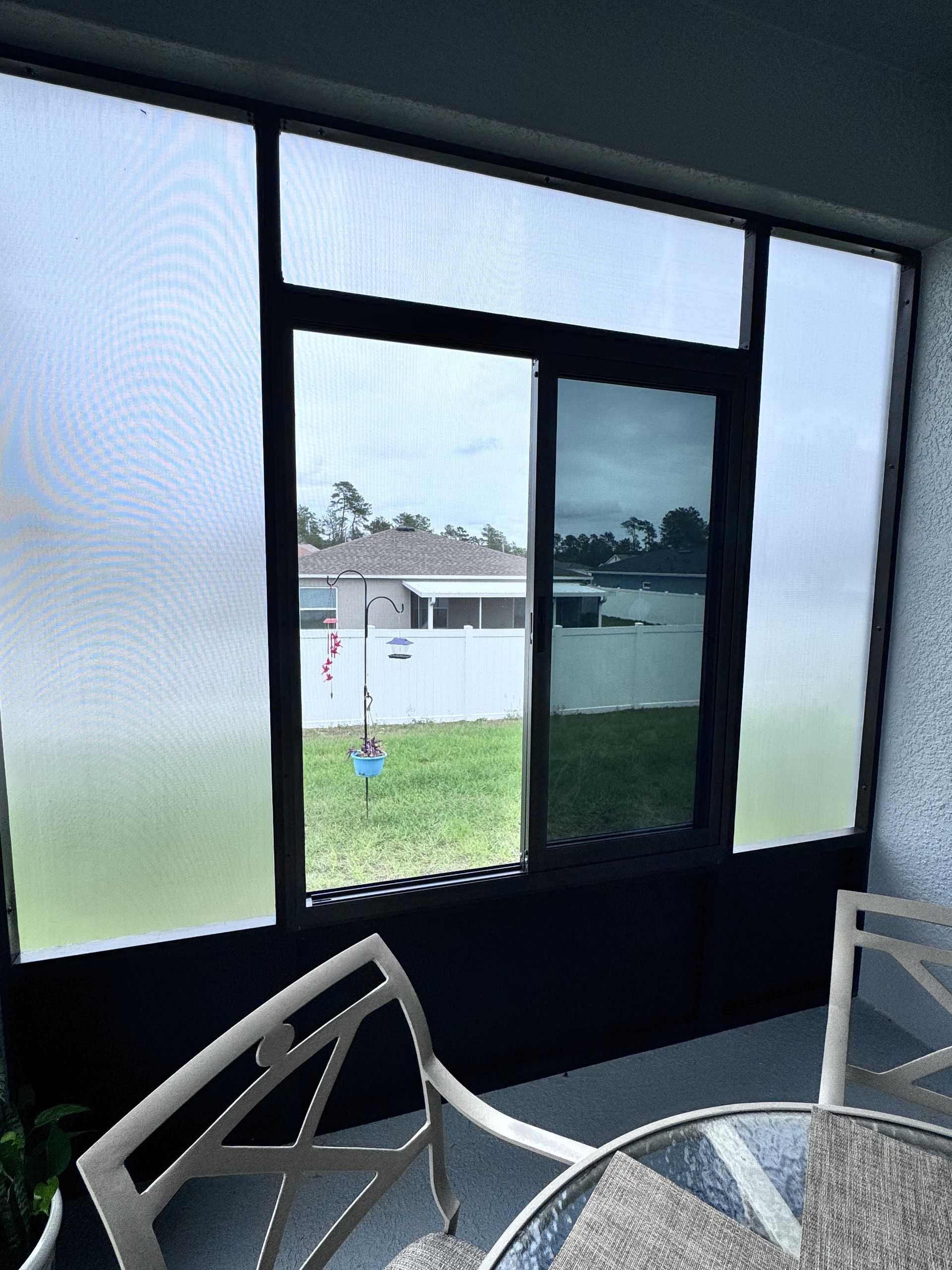 A view through a screened-in porch with a central sliding window looking out onto a backyard and neighboring houses.