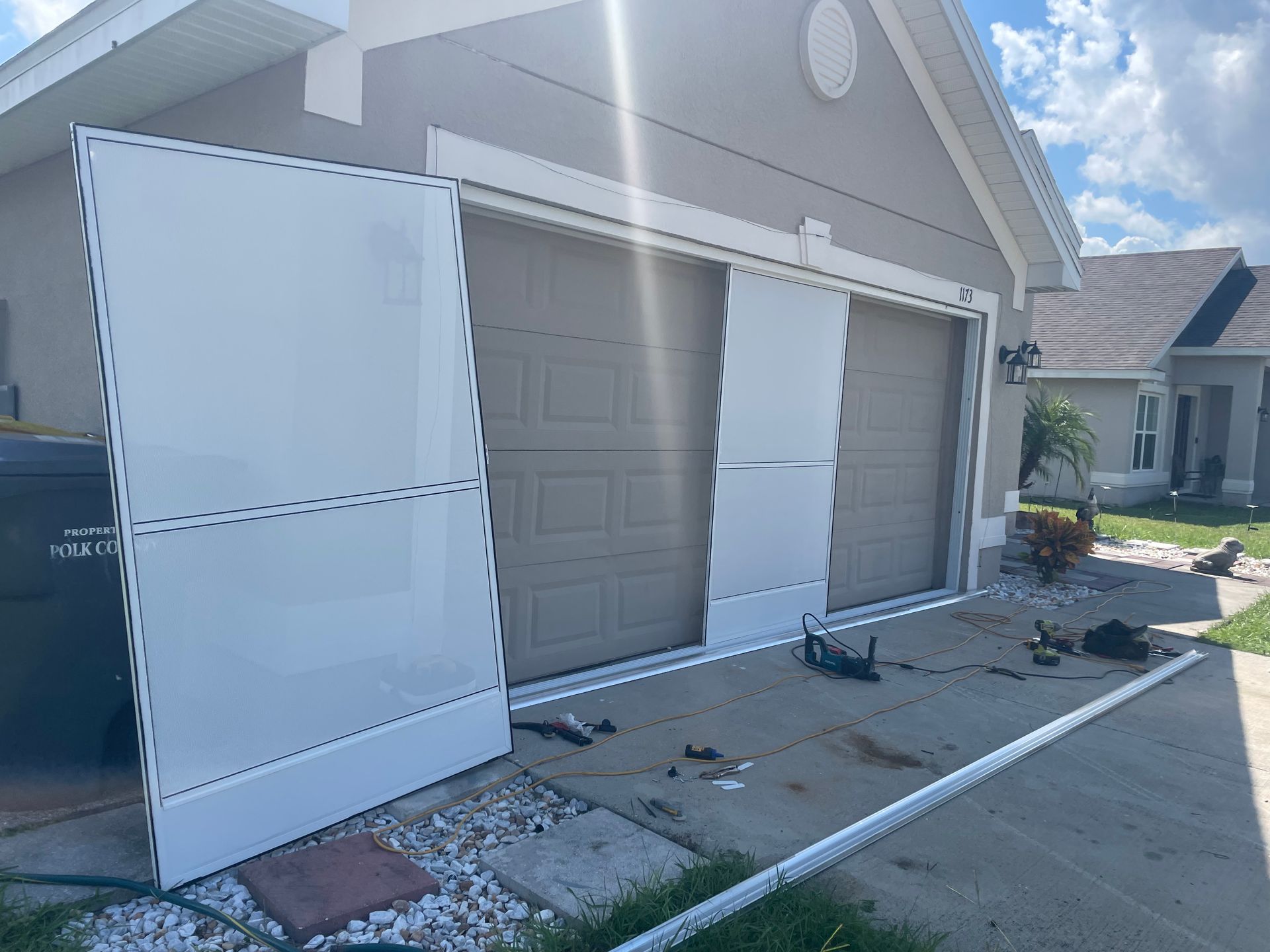 A residential garage with white hurricane shutters being installed on the exterior of the house.