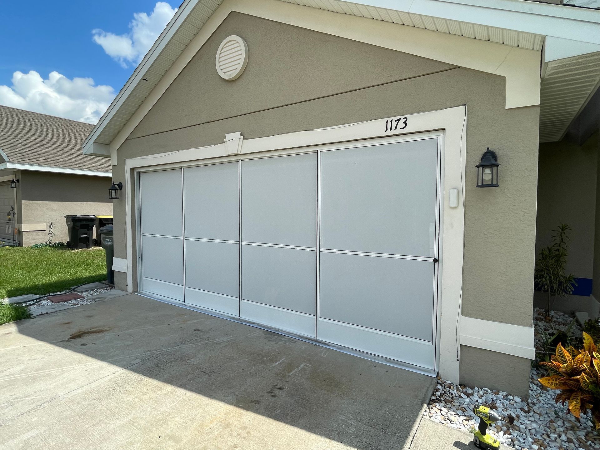 A residential house with a beige garage door featuring a white, framed mesh screen panel under a bright, blue sky.
