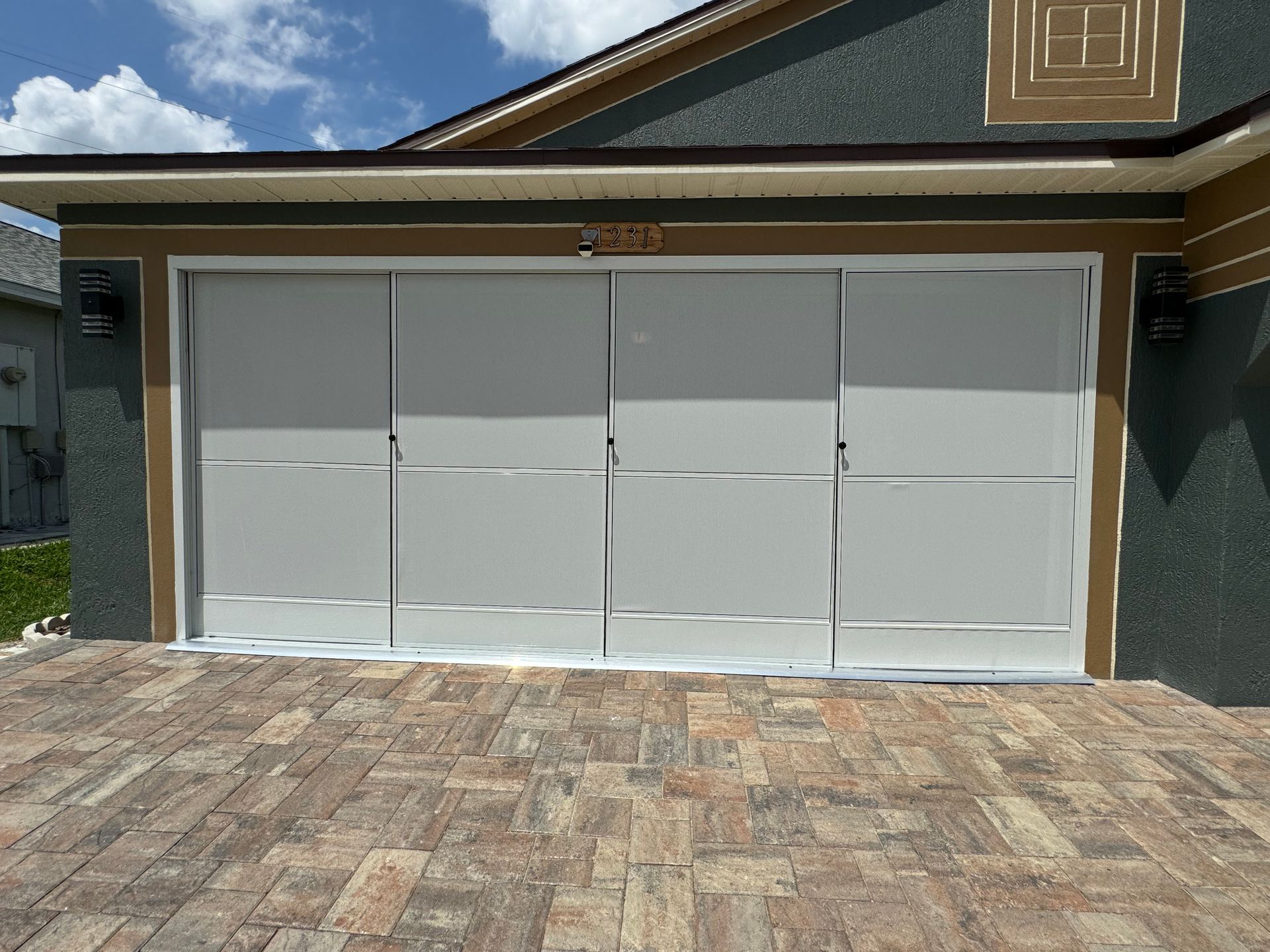 A modern garage door with four white panels, silver horizontal trim, and silver frames set in a dark brown house exterior.