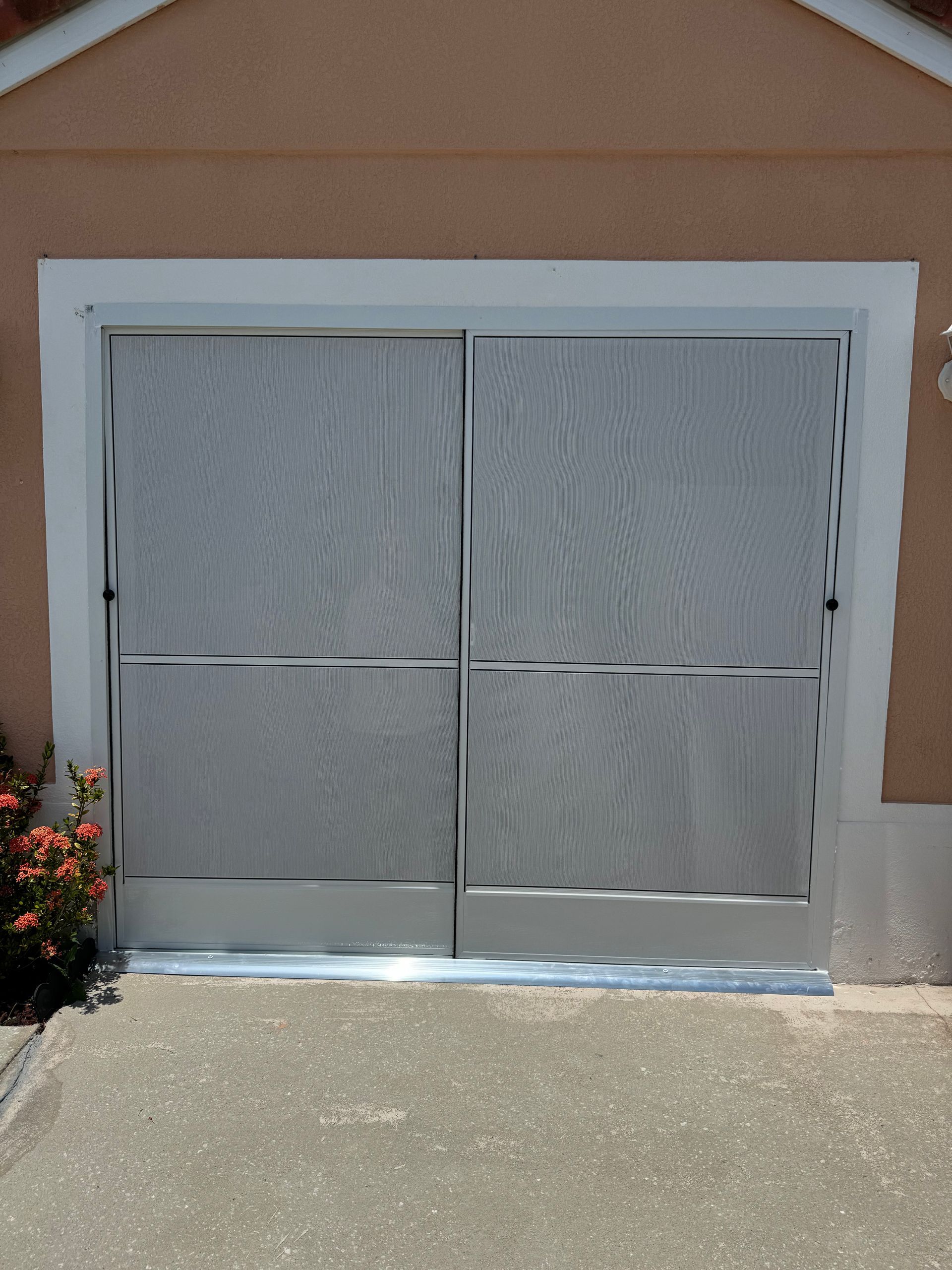 A silver, two-panel mesh garage door screen installed on a beige exterior wall.