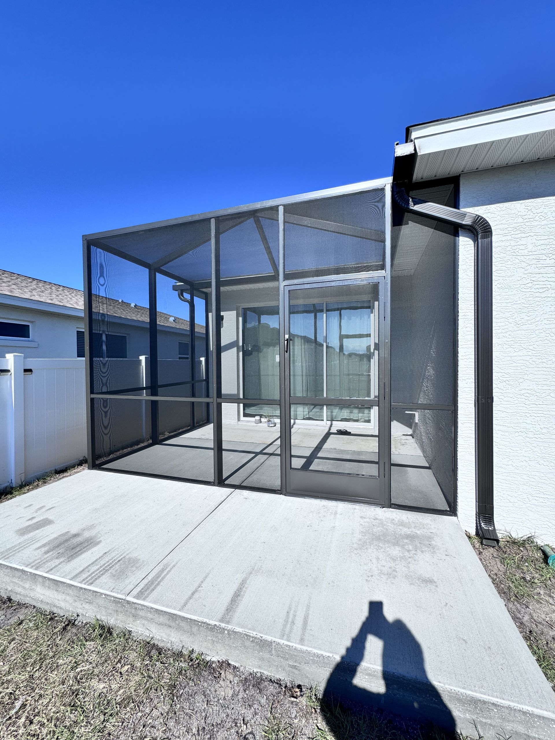 A screened-in patio attached to a light-colored stucco home, featuring a sliding glass door and a concrete slab.