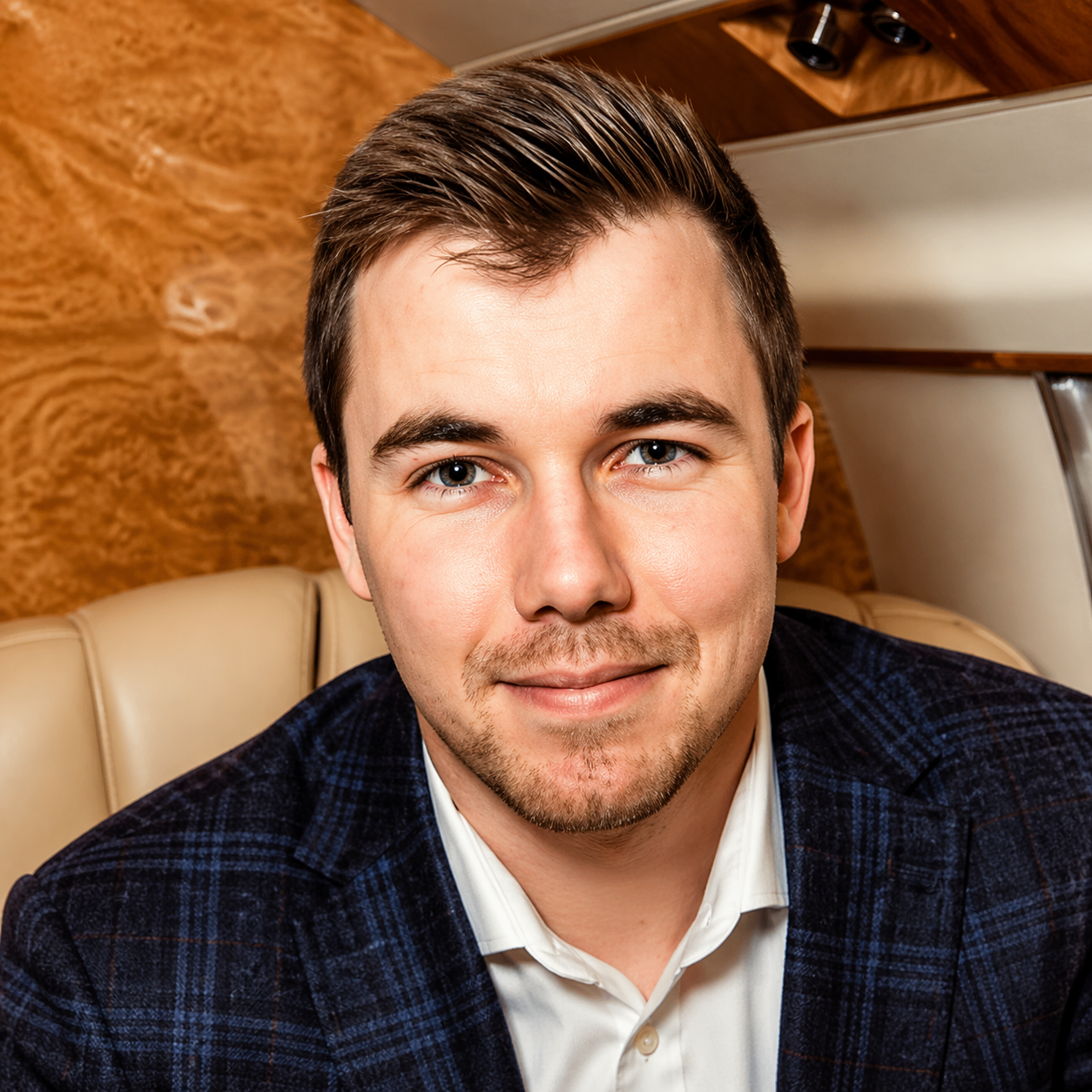 Smiling man in a navy blazer seated in a tan leather seat, with a wood-paneled background