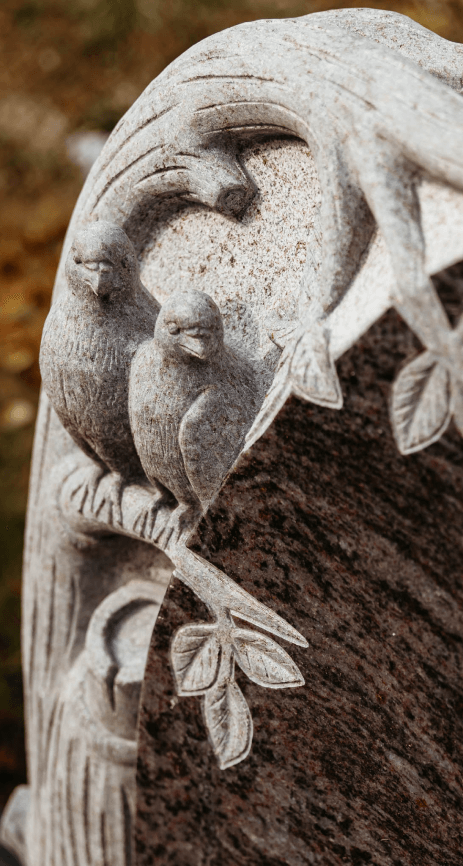 A statue of two birds sitting on a branch on a grave.