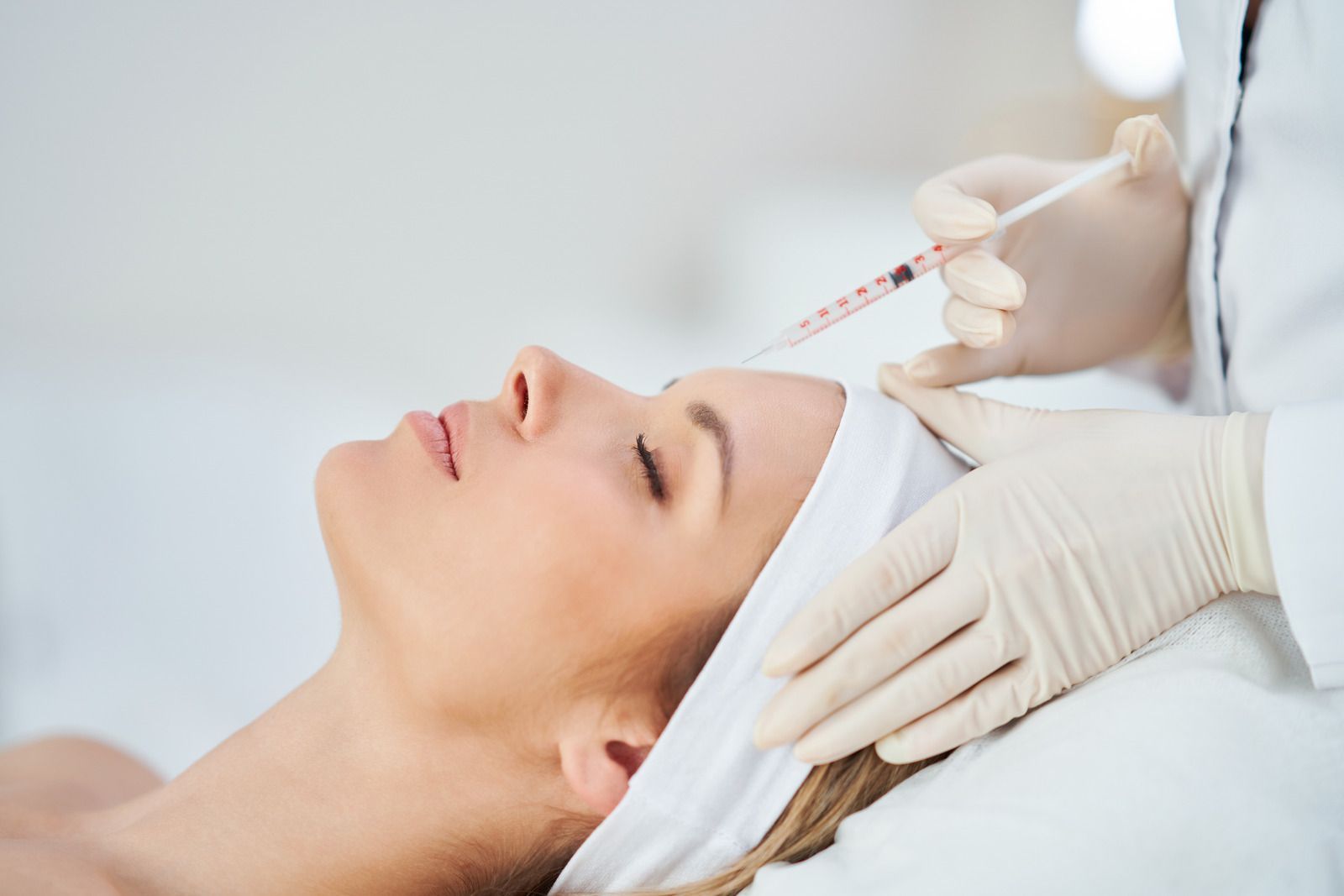 Woman receiving an injection on her forehead. A doctor in gloves holds a syringe.