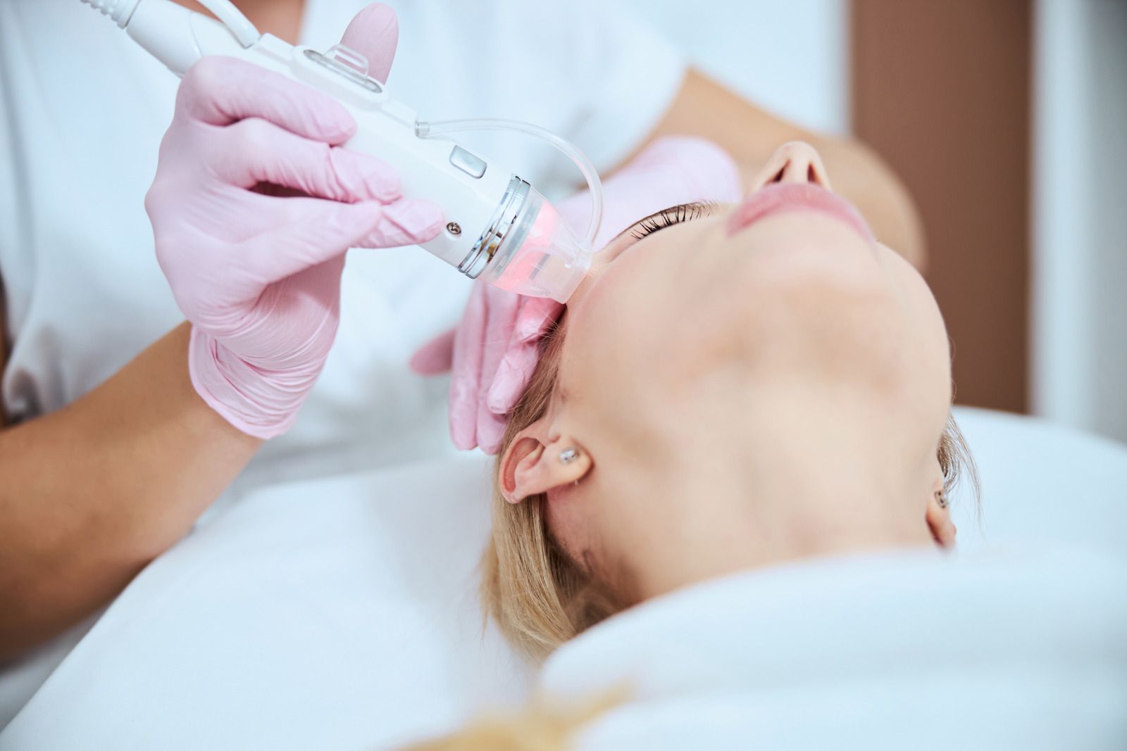 Person receiving facial laser treatment, doctor holding device over face in spa.