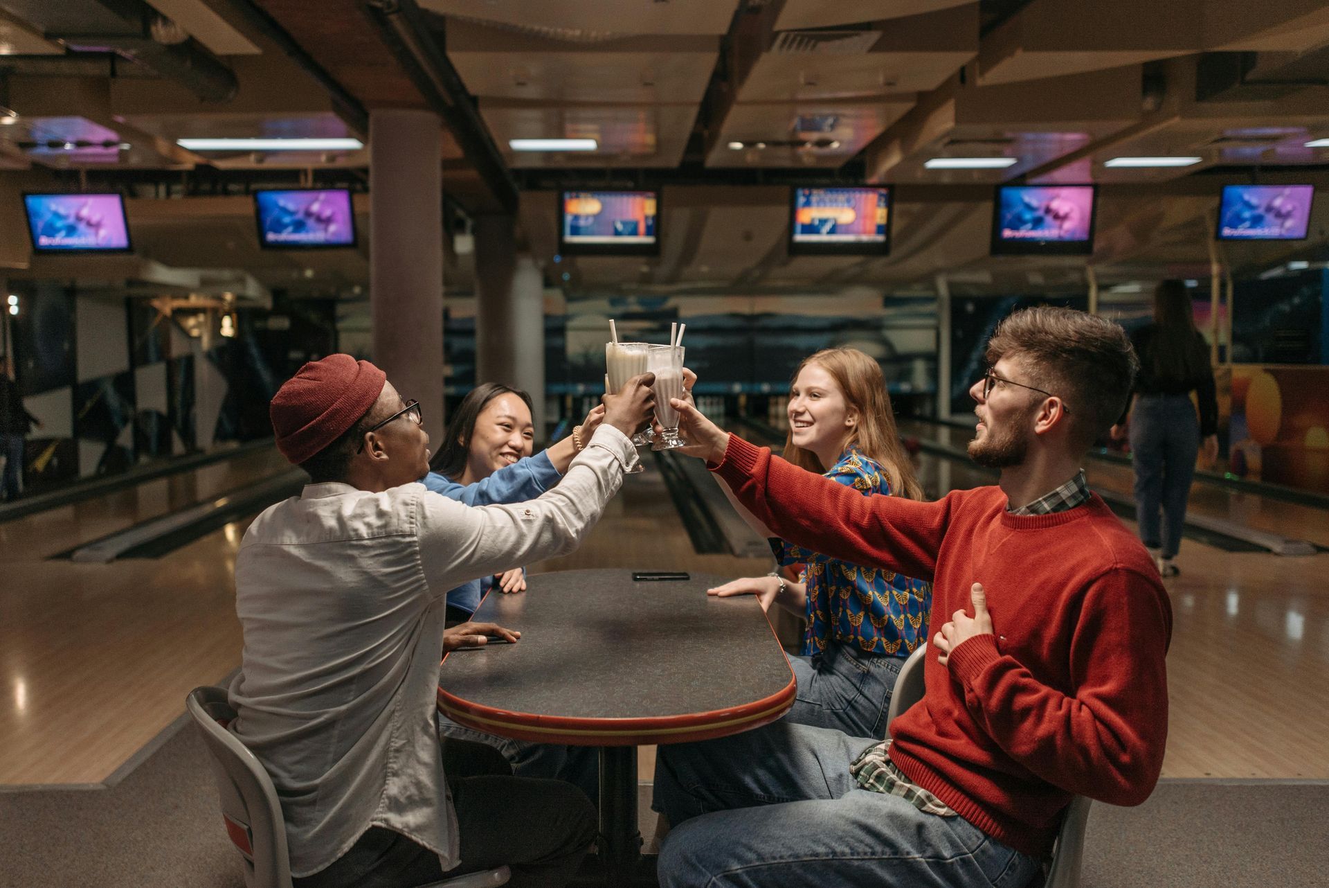 Friends in a bowling alley clinking drinks, smiling.