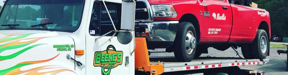 Tow truck carrying a red pickup truck. Both trucks are on a road, daytime.