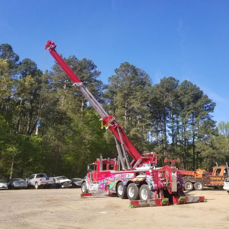 Red tow truck with extended boom against a blue sky, parked on gravel.