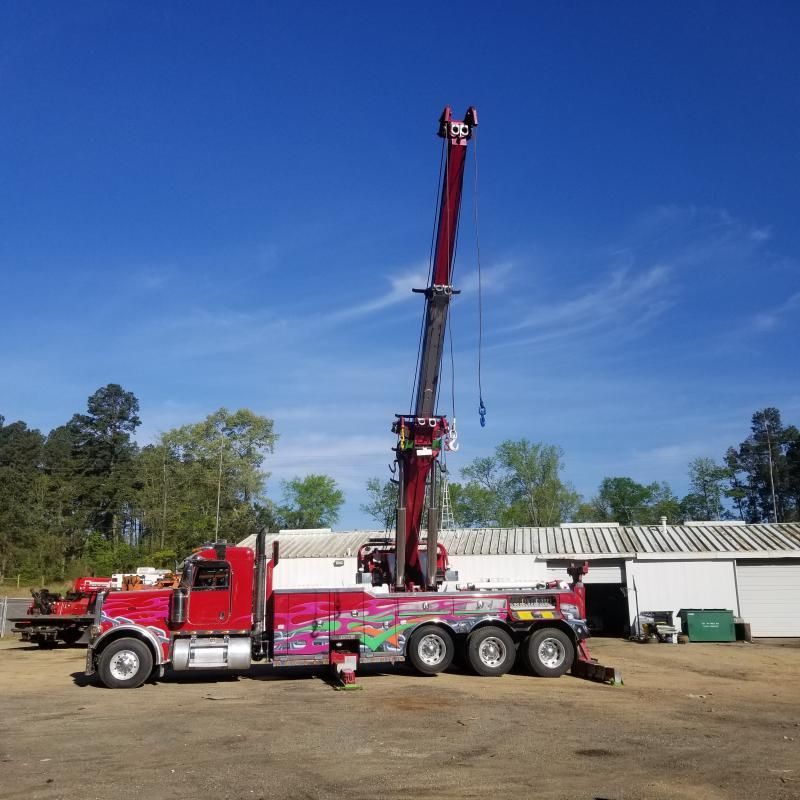 Red tow truck with extended crane, parked outside a building on a sunny day.