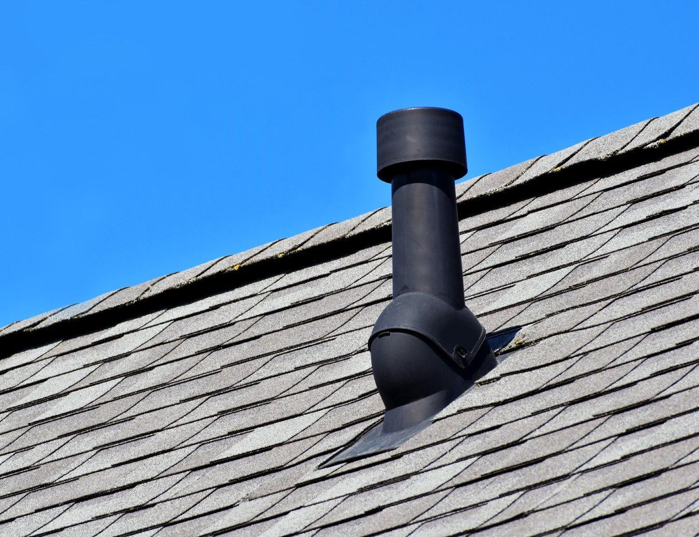 A black chimney on top of a roof with a blue sky in the background.