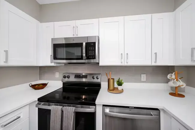 White kitchen with stainless steel appliances, white cabinets, and light gray backsplash.