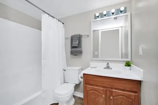 Bathroom with white fixtures, gray walls, and brown vanity. Gray towel hangs by sink.